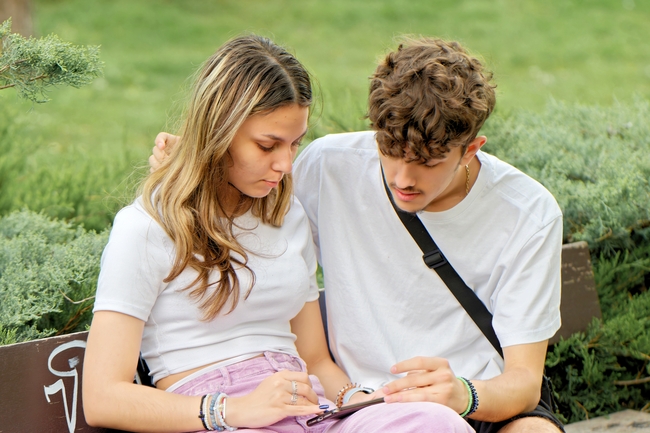 坐在公园椅子上看手机的情侣图片