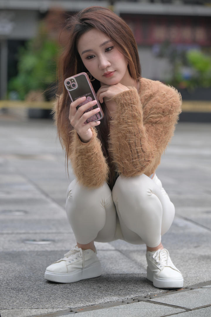 蹲在街上玩手机的紧身裤美女图片