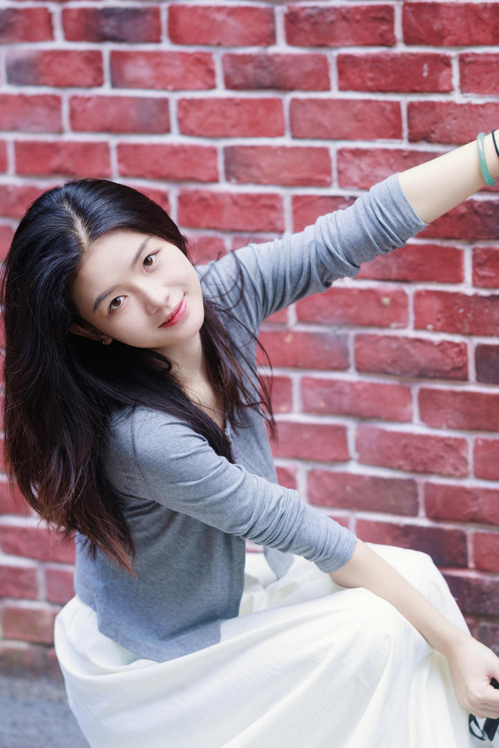 蹲在红墙下的漂亮美女图片大全