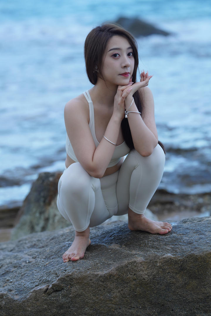 蹲在礁石上的紧身瑜伽裤美女海边人体艺术写真图片